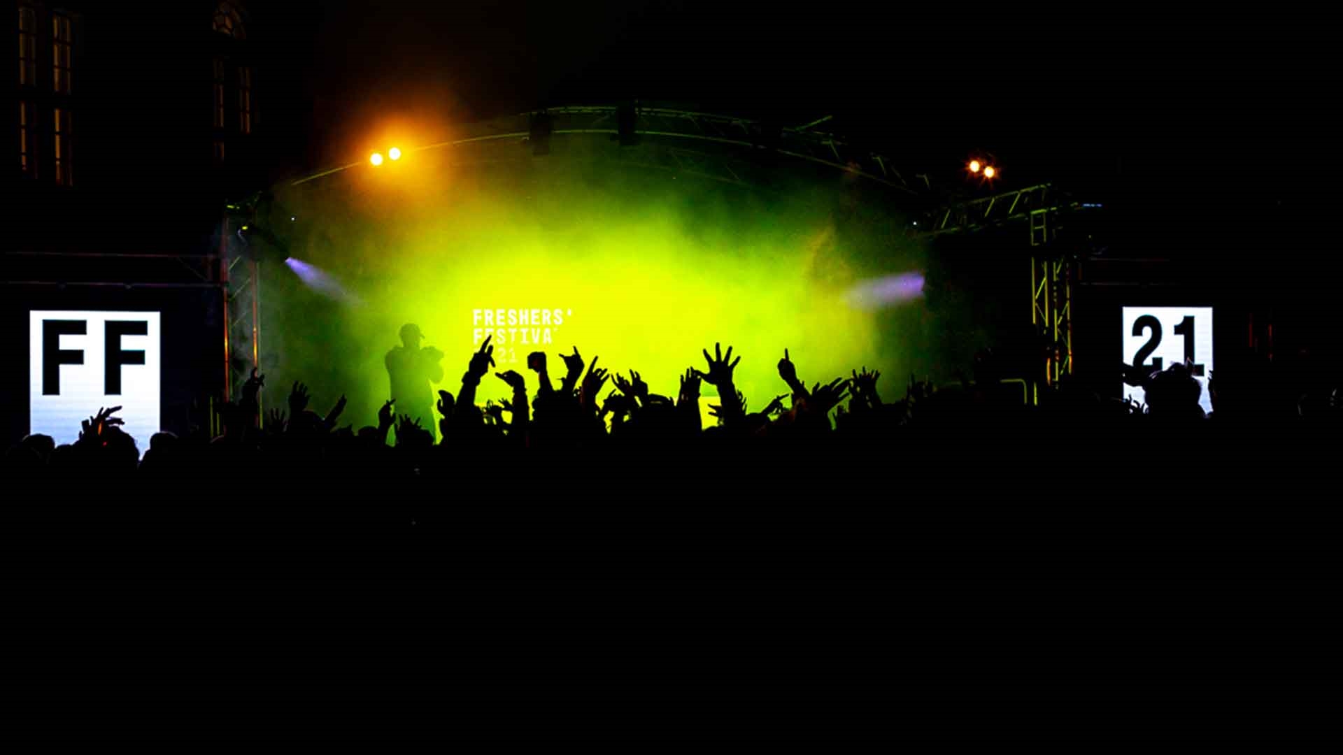 A crowd of people in front of the stage at Freshers Ball 2021, bright green lights are silhouetting the people