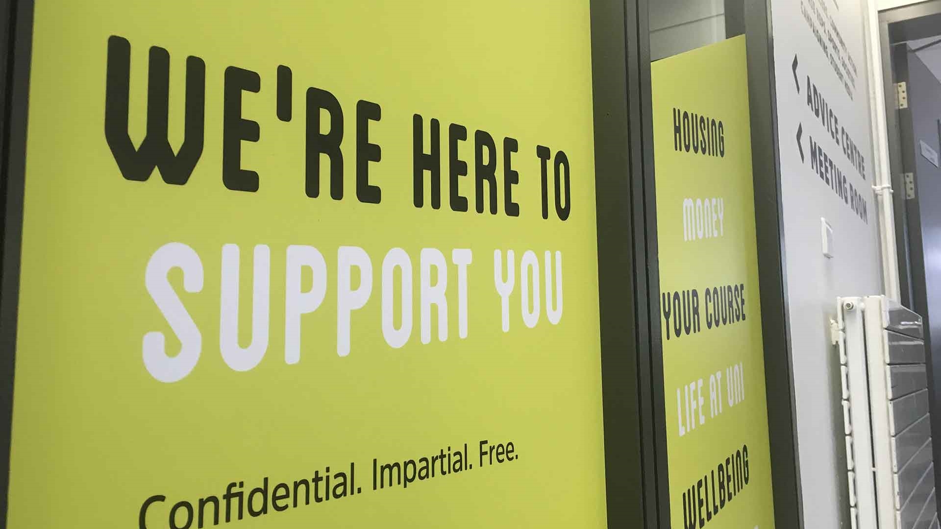A lime green vinyl on the windows of the Advice Centre, the text reads 'we're here to support you'