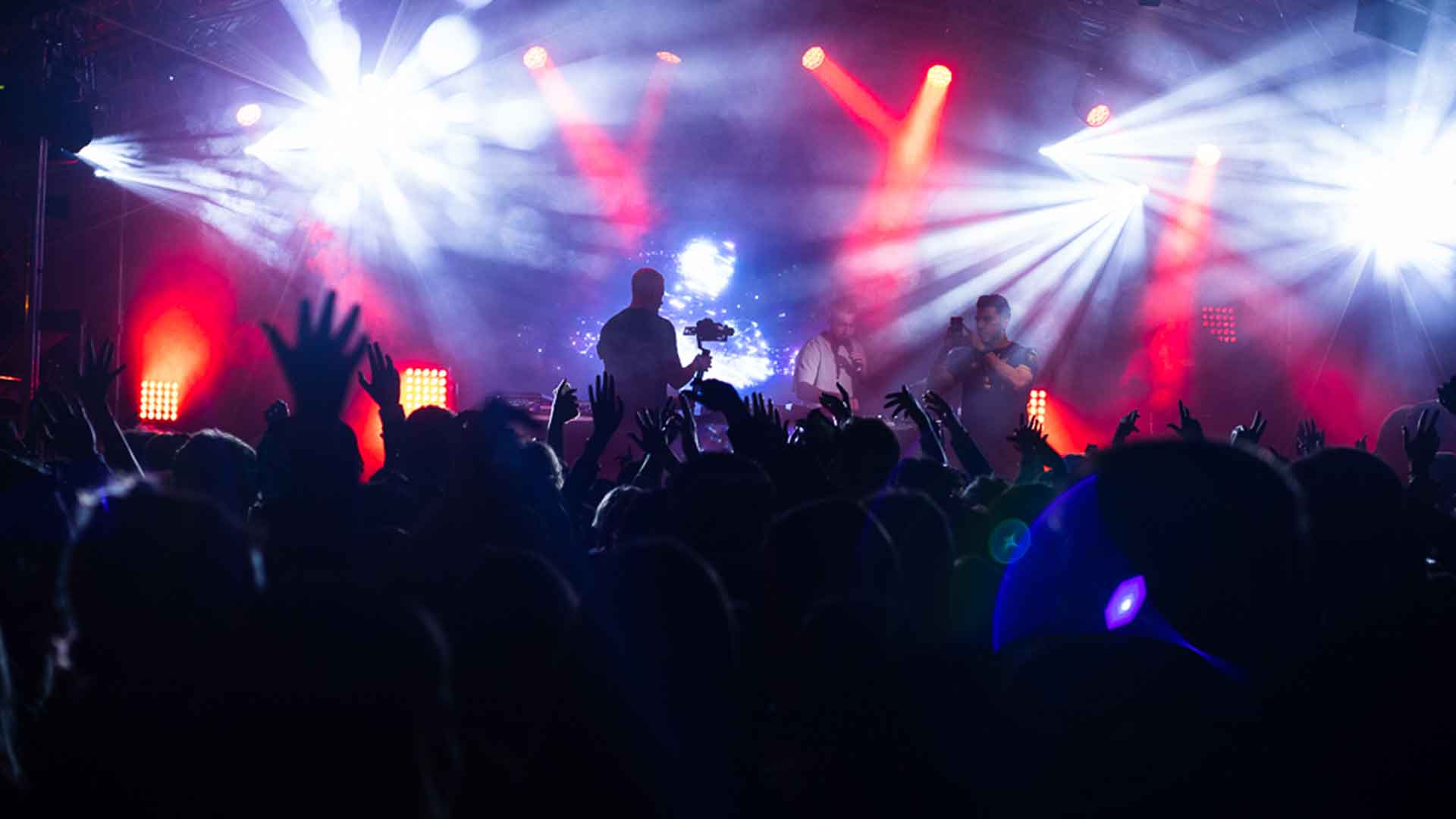 An act on stage taking a photo of the crowd in front of them, the crowd are silhouetted by pink and purple lights