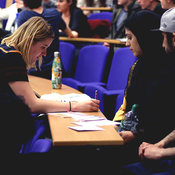 Two people sat at a desk writing on paper