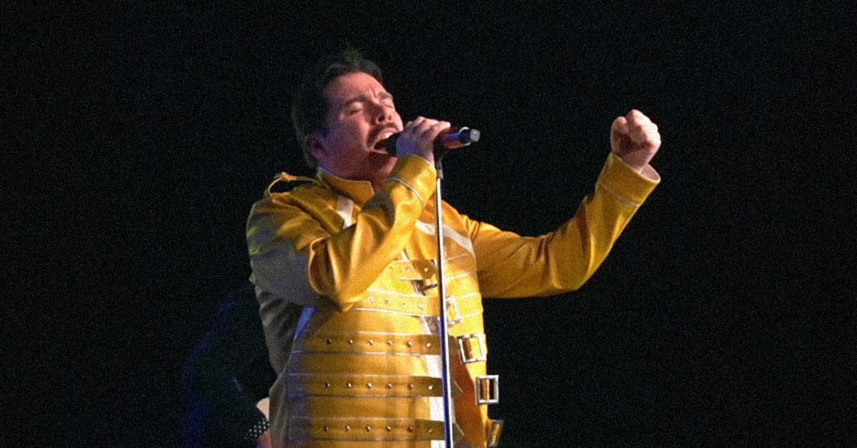 A photo of the singer of Queen Will Rock You, a tribute band, wearing a yellow jacket and singing into a microphone