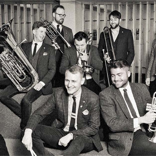 A group of men wearing suits and smiling, holding brass instruments