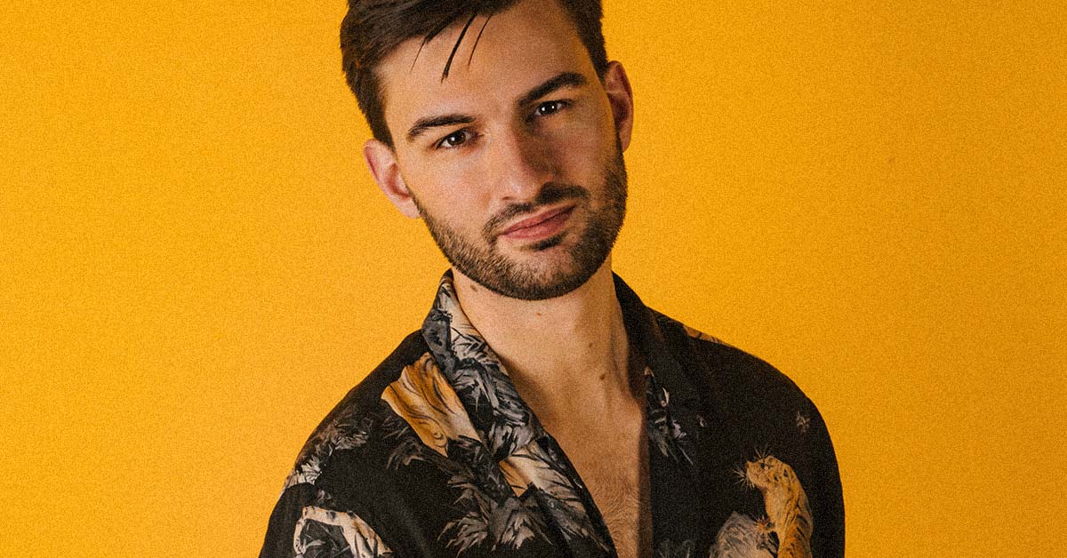 Tom One stood in front of a yellow backdrop wearing a floral shirt