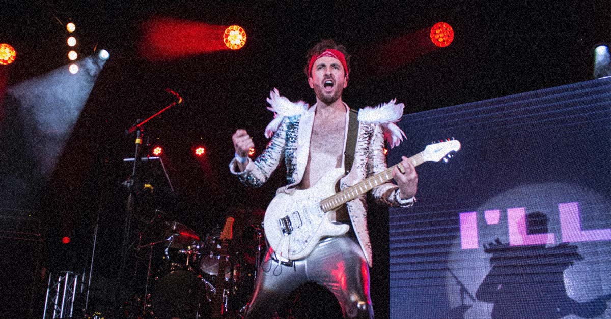A person on a stage wearing a white, glittery, feathery, shiny suit and holding a white guitar