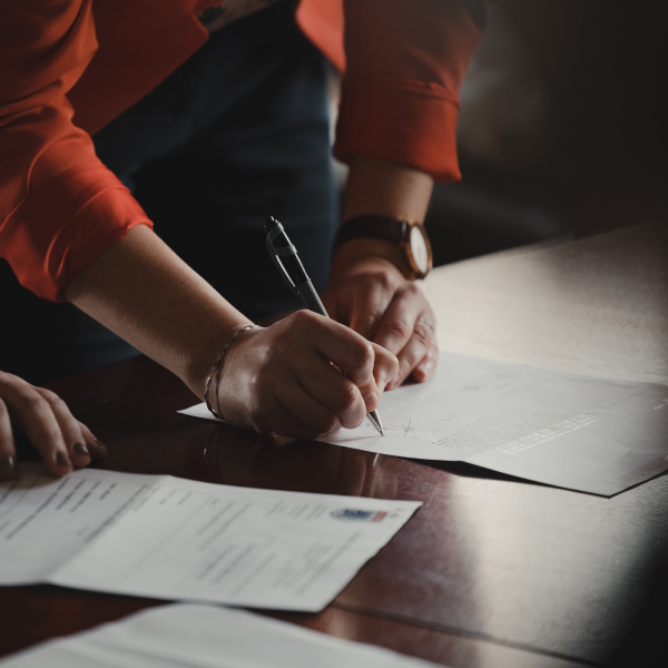 A photograph of two people signing a document. Photo by Romain Dancre on Unsplash.